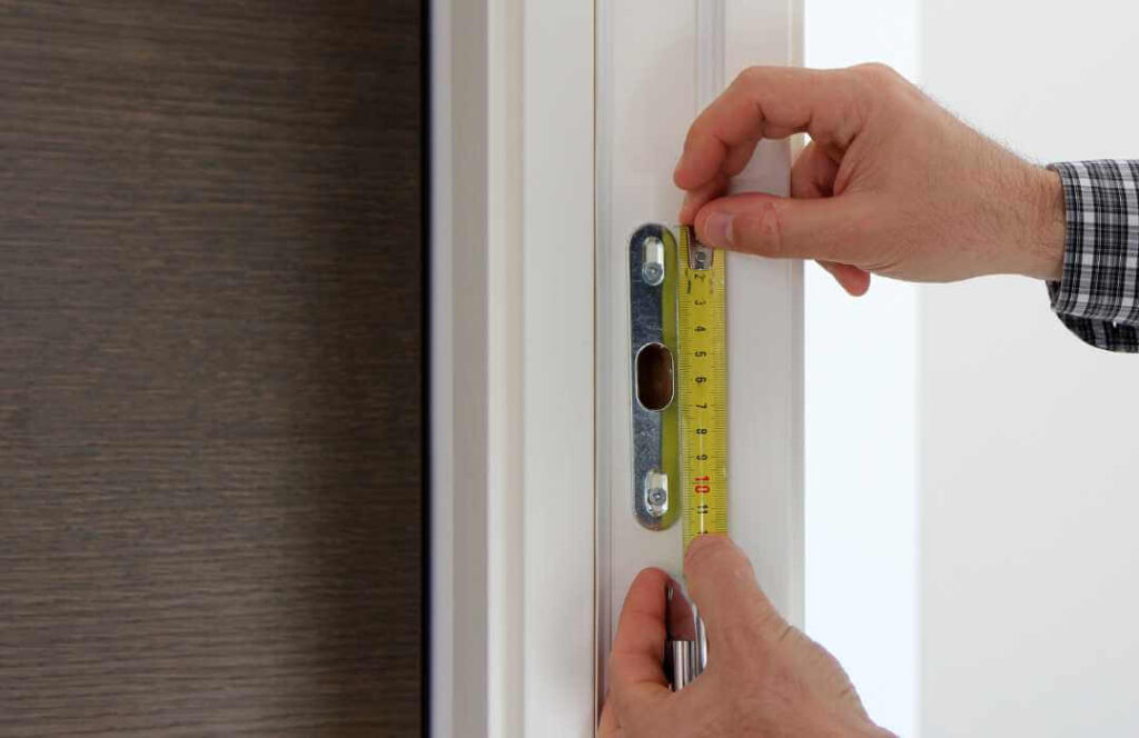 Mierzenie futryny starych drzwi taśmą mierniczą – przygotowanie do montażu nowych drzwi